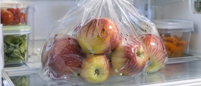 Perforated transparent plastic bag filled with fresh red apples stored neatly on a shelf inside a refrigerator.
